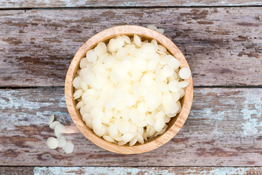 Wooden bowl of white wax flakes on weathered timber