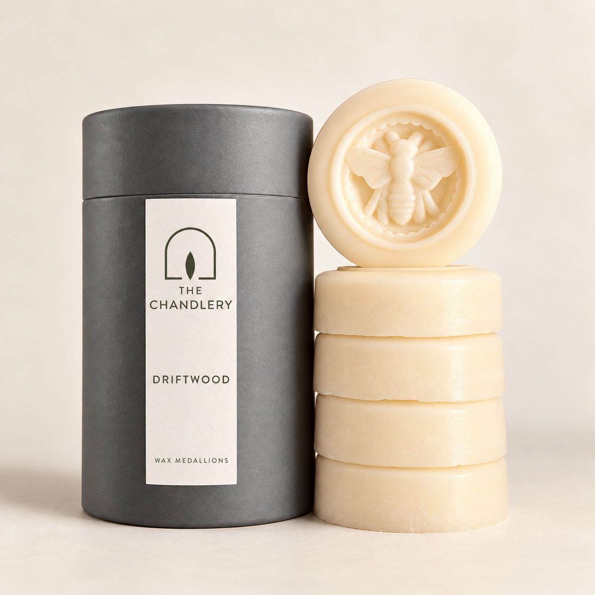 The Chandlery Driftwood wax medallions stacked beside their labelled charcoal tube, with a raised bee design on the top medallion.