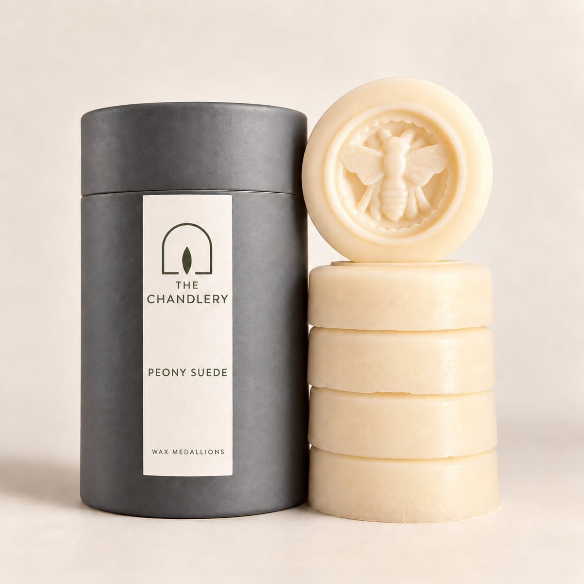 The Chandlery Peony Suede wax medallions stacked beside their labelled charcoal tube, with a raised bee design on the top medallion.