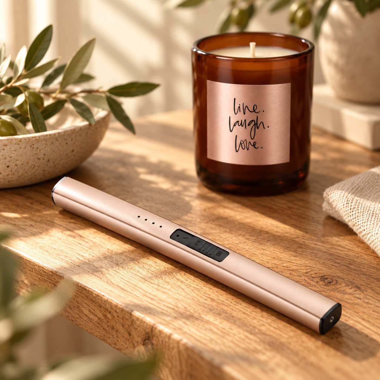 The Chandlery Rose Edit rechargeable lighter beside an amber glass candle on a timber table